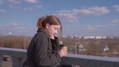 İçkiler ve insanların konsepti. Mutlu genç kadın ya da genç kız. Şehrin arka planında uzun saçlı, şık bir kızla kağıt bardaktan kahve içiyor.