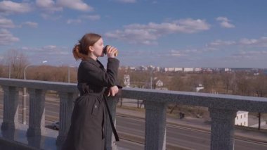 İçkiler ve insanların konsepti. Mutlu genç kadın ya da genç kız. Şehrin arka planında uzun saçlı, şık bir kızla kağıt bardaktan kahve içiyor.