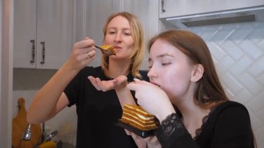 Sıcak aile bağı, anne ve genç bir kızın birlikte lezzetli bir ballı pasta yiyip, parlak, modern bir mutfak alanında güzel bir anın tadını çıkarmasıyla ortaya çıkar.