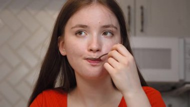 Genç kız, dizüstü bilgisayarında çalışırken kahvaltı ve içkinin keyfini çıkarıyor. Evde, mutfak masasında pencere kenarında rahatça oturuyor. Video aracılığıyla iletişim kuruyor.