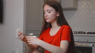 Genç kız, modern mutfakta cam masada oturmuş, her sabah yoğurdun tadını çıkarıyor, sağlıklı yaşam tarzını ve sağlığını temsil ediyor.