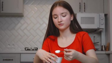 Genç kız, modern mutfakta cam masada oturmuş, her sabah yoğurdun tadını çıkarıyor, sağlıklı yaşam tarzını ve sağlığını temsil ediyor.