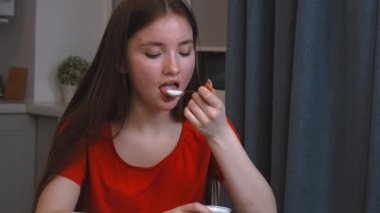 Genç kız, modern mutfakta cam masada oturmuş, her sabah yoğurdun tadını çıkarıyor, sağlıklı yaşam tarzını ve sağlığını temsil ediyor.