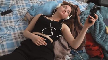 Rahatlamış genç bir kız yatağında dinleniyor, kulaklık takıyor, oyun seansından sonra müzikten keyif alıyor, evinde huzurlu bir dinlenme anını kişileştiriyor.