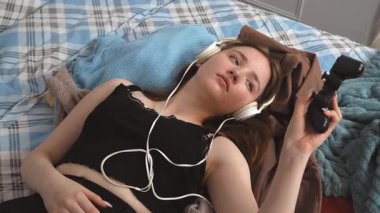 Rahatlamış genç bir kız yatağında dinleniyor, kulaklık takıyor, oyun seansından sonra müzikten keyif alıyor, evinde huzurlu bir dinlenme anını kişileştiriyor.