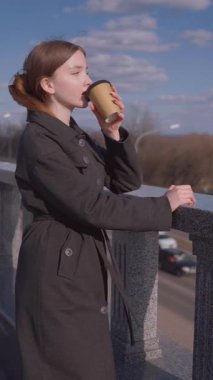 İçkiler ve insanların konsepti. Mutlu genç kadın ya da genç kız. Şehrin arka planında uzun saçlı, şık bir kızla kağıt bardaktan kahve içiyor.