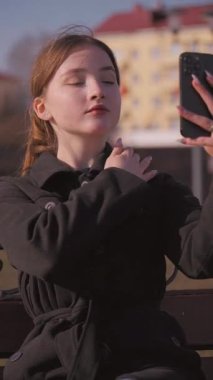 Kentsel yaşam tarzı kavramı, şehir manzarasına tepeden bakan bir balkonda kahve içerken fotoğraf çeken ya da telefonuyla video kaydeden genç bir kız tarafından örneklendirilir.