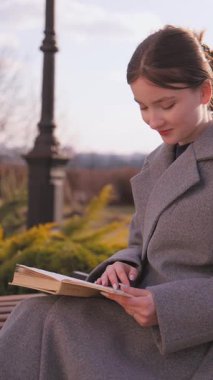 Edebiyat okuyan bir öğrenci dikkatlice okur, rahatça parkta bir bankta oturur, sakin doğayla çevrili bir kitabın sayfalarını çevirir.