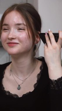 Genç kız, modern mutfaktaki akıllı telefondan sesli mesajları dinlerken rahat bir şekilde kablosuz teknoloji videosuna bağlanıyor.