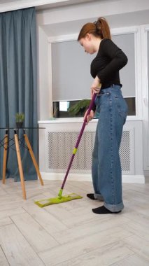 Genç kız ev hanımı mutfak zeminini temizlerken paspas kullanıyor, Parlak, modern apartman içinde lekesiz yüzeyleri korumaktan memnuniyet duyuyor.