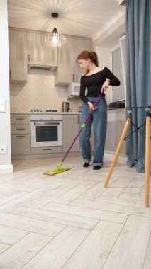 Genç kız ev hanımı mutfak zeminini temizlerken paspas kullanıyor, Parlak, modern apartman içinde lekesiz yüzeyleri korumaktan memnuniyet duyuyor.