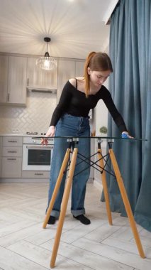 Genç kız cam masa yüzeyini iyice temizliyor, modern mutfak içinde kusursuz parlaklık sağlıyor, titiz hijyen ve ev işleri hassasiyetini gösteriyor.