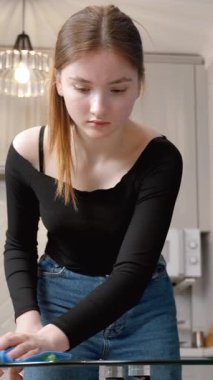 Genç kız cam masa yüzeyini iyice temizliyor, modern mutfak içinde kusursuz parlaklık sağlıyor, titiz hijyen ve ev işleri hassasiyetini gösteriyor.