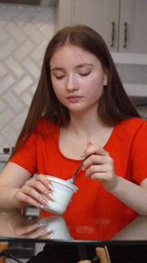 Genç, cam masada oturmuş, günlük evde besleyici atıştırmalıkların tadını çıkarırken,... kaymak gibi yoğurdun tadını çıkarıyor.