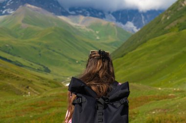 Sırt çantalı genç yürüyüşçü dinleniyor ve Gürcistan 'daki Kafkas dağlarının karlı tepelerinin manzarasının tadını çıkarıyor.