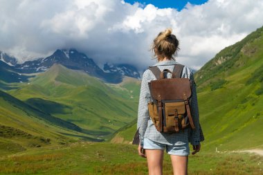 Sırt çantalı kadın yürüyüşçü, Gürcistan 'ın svaneti bölgesindeki kar kaplı dağların ve yeşil vadilerin çarpıcı manzarasının keyfini çıkararak doğanın güzelliğini ve macera ruhunu gözler önüne seriyor.
