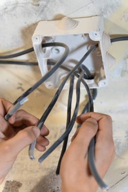 Elektrikçi, ev tadilatı sırasında elektrik kablolarını bir bağlantı kutusuna dikkatlice bağlayıp güvenli ve güvenilir elektrik bağlantıları sağlıyor. Dikey fotoğraf