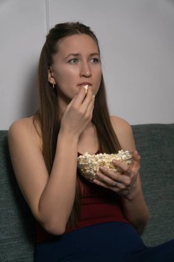 Genç bir kadın rahat bir koltukta oturur, bir filme dalmışken cam kaseden patlamış mısırın tadını çıkarır, evinde rahat ve rahatlatıcı bir akşam geçirir. Dikey fotoğraf