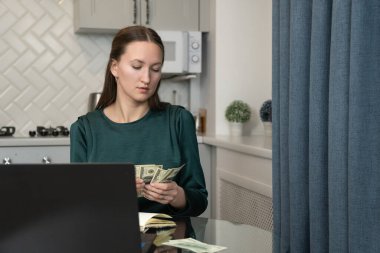 İş kadını ofisteki cam masada oturuyor, bize dolar banknotları sayıyor, yakınlarda dizüstü bilgisayarları ve defterleri var, ev finansmanlarını, bütçe hesaplarını veya hesaplama yatırımlarını yönetiyor.