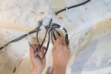 Elektrikçi ev tadilatı sırasında elektrik kablolarını bir bağlantı kutusuna dikkatlice bağlıyor ve güvenli ve güvenilir elektrik bağlantıları sağlıyor.