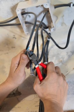 Elektrikçi, elektrik sistemindeki güvenli ve verimli bağlantıları sağlamak için penseyi ustalıkla keserek elektrik kablolarını soyuyor, hayati bakım ve montaj işlerini yapıyor.