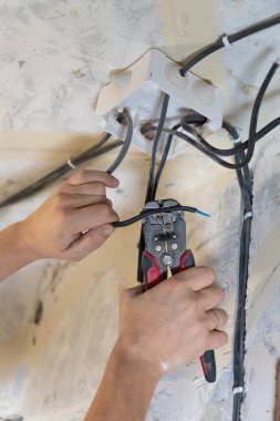 Elektrik tesisatı üzerinde çalışan elektrikçi, bir ev yenileme veya inşaat projesi sırasında bağlantı kutusuna kabloları dikkatlice hazırlamak için tel sökücüleri kullanıyor. Dikey fotoğraf