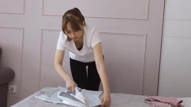 Genç kadın ev işlerini etkili bir şekilde yönetiyor, yatak odasındaki çamaşırları dikkatlice ütülüyor ve katlıyor, ev işlerini ve organizasyon becerilerini gösteriyor.