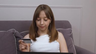 Kadın rahat bir şekilde dizüstü bilgisayarda çalışıyor, evde dinlenirken kredi kartı kullanarak güvenli online ödeme işliyor, modern dijital bankacılık kolaylığını temsil ediyor.