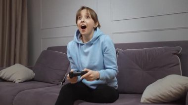 Hevesli oyuncu zaferi kutluyor, konsolda bilgisayar oyunu oynarken saf mutluluğu ifade ediyor, keyifli ve rahat bir oturma odasında zaferin animasyon tepkilerini gösteriyor.