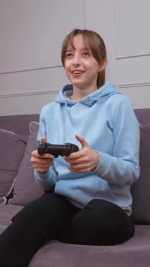 Hevesli bir oyuncu zaferi kutluyor, konsolda video oyunu oynarken saf mutluluğu ifade ediyor, keyifli ve zafer dolu bir oturma odasında dikey bir video klipte canlandırılmış tepkiler gösteriyor.