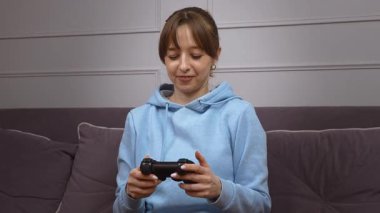 Oyun oynayan genç bir kadın, elinde kontrolörle zaferi kutlarken oturma odasında kanepede oturup oyun seansını kazanmanın sevincini ve heyecanını dile getiriyor.