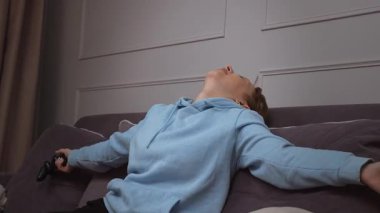 Hevesli oyuncu zaferi kutluyor, konsolda bilgisayar oyunu oynarken saf mutluluğu ifade ediyor, keyifli ve rahat bir oturma odasında zaferin animasyon tepkilerini gösteriyor.