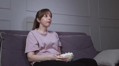 Genç bir kadın rahat bir koltukta oturuyor, sinemadan zevk alıyor ve cam bir kaseden patlamış mısır yiyor, değişik şaşkınlık ve eğlence ifadeleri sergiliyor.