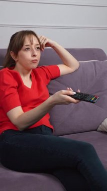 Oturma odasındaki kanepede uzanan bir kadın, en sevdiği TV programının keyfini çıkarıyor. Rahatlamış, kaygısız, akşam keyfi, dikey videosu olan bir kadın.