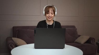 Uzaktan çalışan, kulaklık takan ve arka planda mor kanepesi olan minimalist beyaz ofis bilgisayarında daktilo yazan mutlu, mutlu ve mutlu bir profesyonel.