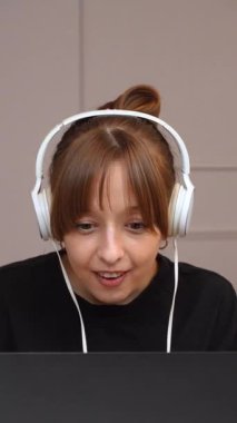 Uzaktan çalışan, kulaklık takan ve dizüstü bilgisayarda arka planda mor kanepe ve dikey videoda minimalist beyaz ofis bilgisayarında yazan mutlu, mutlu ve mutlu bir profesyonel.