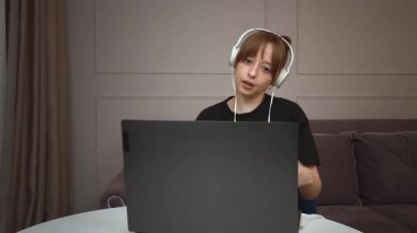 Uzaktan çalışan, kulaklık takan, ev bilgisayarında yazı yazan genç bir kadın uzman dijital çalışma gününde odaklanmış ve üretken davranışlar sergiliyor.