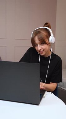 Uzaktan çalışan, dizüstü bilgisayarla yazarken dikkatle odaklanan, kulaklık takan ve dairedeki rahat dairenin içindeki yuvarlak masada oturan serbest çalışan bir kadın.