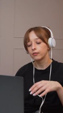 Evde çalışan, kulaklık takan ve bilgisayarındaki video konferansında konuşan genç iş kadını farklı ifadeler ve jestler gösteriyor.