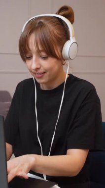 Evde çalışan, kulaklık takan ve bilgisayarındaki video konferansında konuşan genç iş kadını farklı ifadeler ve jestler gösteriyor.