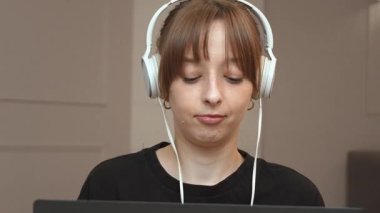 Müzik dinlerken kulaklık takan genç bir profesyonel, minimalist iç dekorasyonda hafif şüpheli ifadeyle dizüstü bilgisayarda çalışıyor.