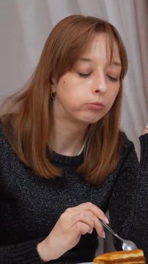 Katmanlı ballı pastanın tadını çıkaran genç bir kadın. Parlak, çağdaş beyaz bir mutfakta otururken kaşıkla narin ısırıkların tadını çıkaran bir kadın. Mutfak zevki ve kişisel rahatlama anı.