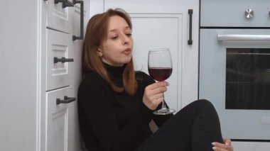 Yalnız bir kadın mutfak zemininde oturmuş, kırmızı şarap içiyor, duygusal çöküntü yaşıyor ve yalnızlık anı ile derin kişisel mücadeleler veriyor.