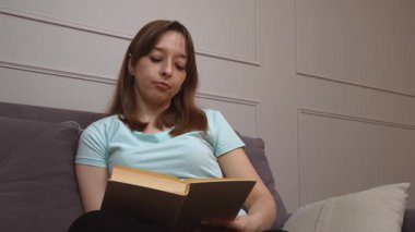 Bir kadın rahat bir şekilde kanepede oturup kitap okumaktan, duruşunu ve yüz ifadelerini değiştirmekten, sakin, huzurlu bir tavırla, sakin bir kişisel rahatlık anında, keyif almaktan hoşlanır.