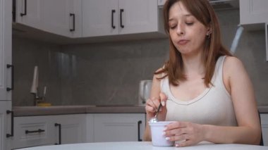 Genç bir kadın kremalı yoğurdun tadını çıkarıyor. Mutfak ortamında lezzet tadarken saf zevki tadıyor. Keyifli tepkisi sayesinde gerçek bir zevk veriyor.