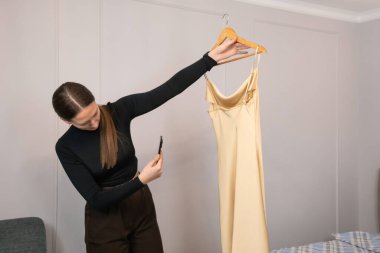 Moda tasarımcısı ahşap bir askıda şık bir elbise görüntüsü yakalıyor, çevrimiçi bir mağazada satışa hazırlanıyor, yaratıcılığı e-ticaret başarısı için modern teknolojiyle harmanlıyor.