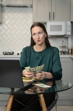 Genç iş kadını evinden işine odaklanıyor, mutfak masasında dizüstü bilgisayar ve defterle otururken internetten kazandığı paraları sayıyor, hesaplarını incelikle yönetiyor. Dikey fotoğraf