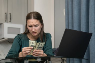 Evde dizüstü bilgisayarla son dolarlarını hesaplayan genç bir kadın. Tahliye ve iş kaybıyla karşı karşıyayken maddi açıdan stresli ve çaresiz hissediyor.