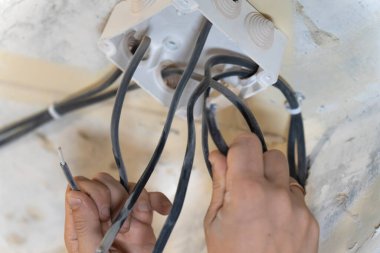 Elektrikçi ev tadilatı sırasında elektrik kablolarını bir bağlantı kutusuna dikkatlice bağlıyor ve güvenli ve güvenilir elektrik bağlantıları sağlıyor.