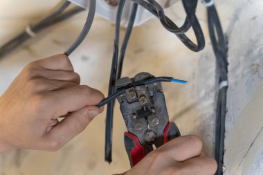 Elektrikçi, elektrik kablosundan yalıtım malzemelerini dikkatlice çıkarmak için kablo sökücüleri kullanıyor. Ev yenileme projesi sırasında bağlantı için hazırlıyor.